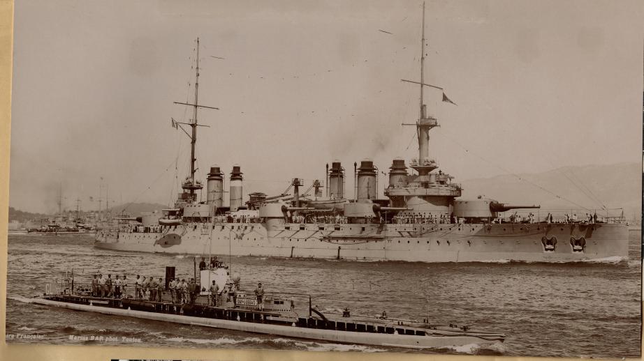 Photo noir et blanc du début du 20ème siècle. Au premier plan un sous marin en surface au second le Cuirassé Danton. Tous deux naviguent de conserve