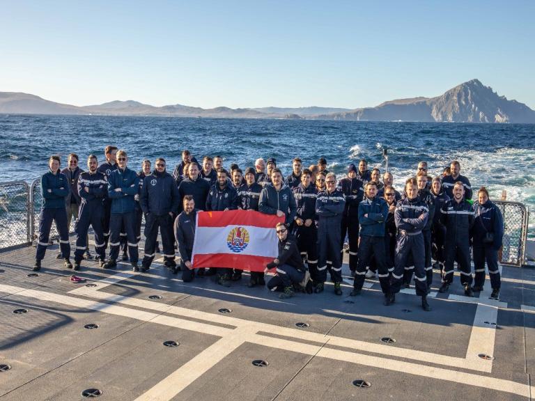 L'équipage du patrouilleur outre-mer sur la plage arrière avec le drapeau du bâtiment
