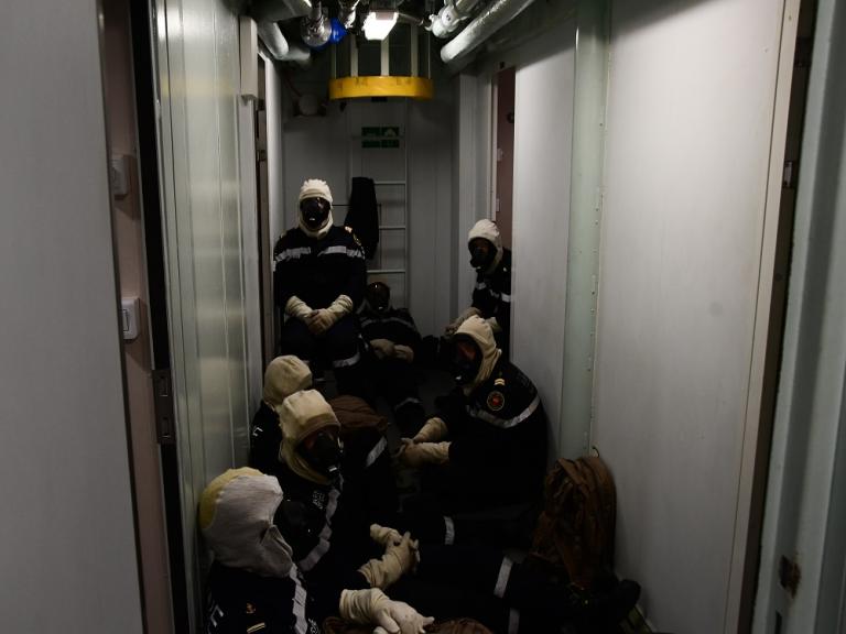 Des marins s'entraînent dans les coursives de la frégate Aquitaine en tenue de feu