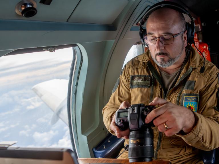 Un photographe en tenue de vol consulte son appareil dans un avion