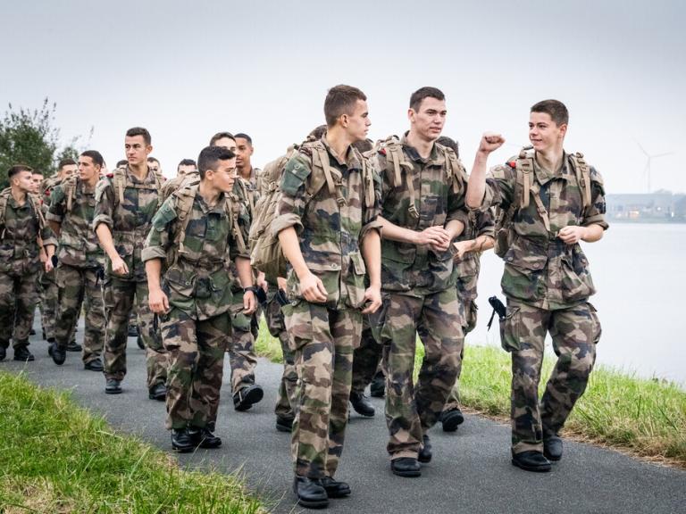 Un groupe de soldats en treillis marche au bord d'une route